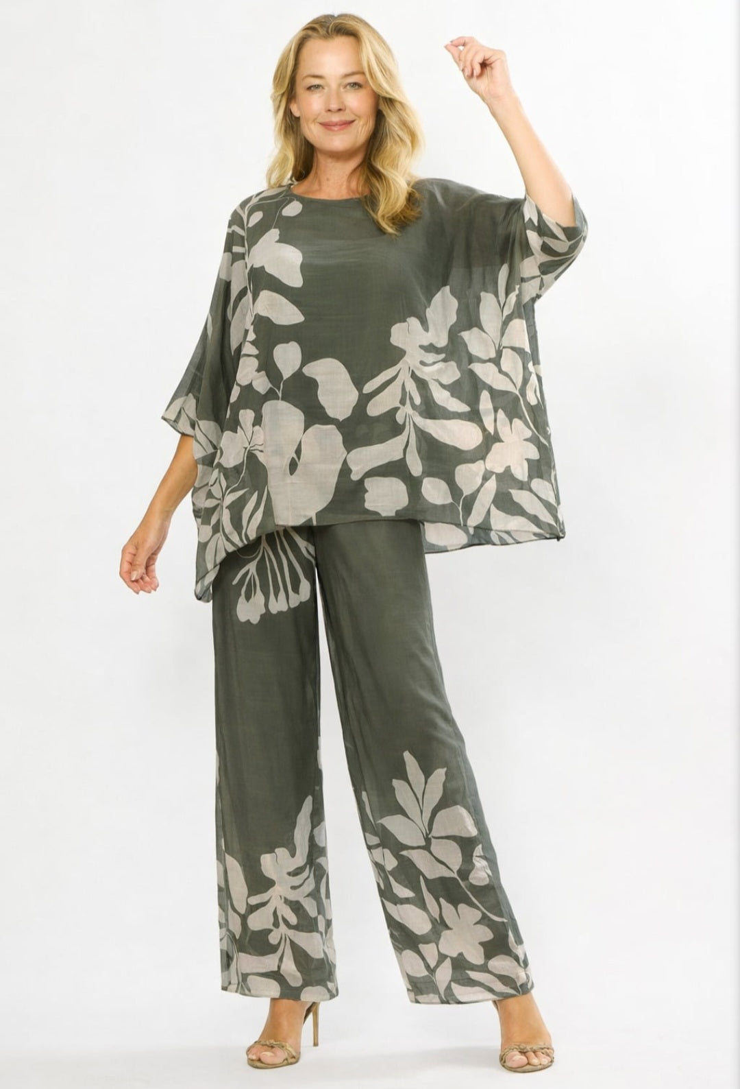 A woman modeling a matching two-piece lounge set featuring a loose, short-sleeve top and wide-leg pants in olive green with a large light gray floral print, set against a plain white studio background.