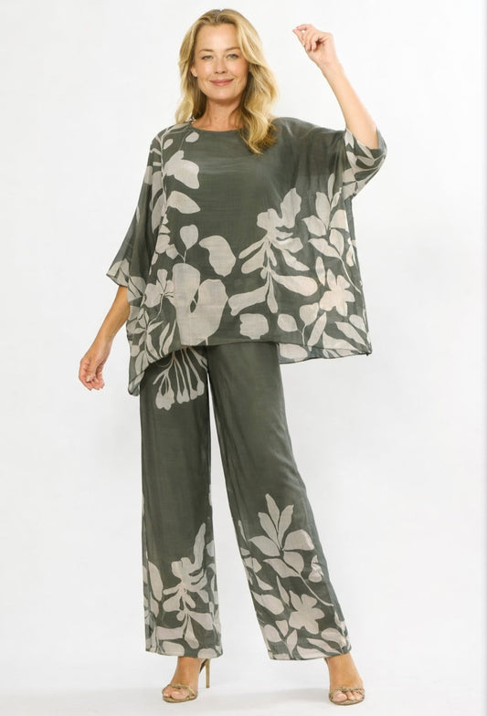 A woman modeling a matching two-piece lounge set featuring a loose, short-sleeve top and wide-leg pants in olive green with a large light gray floral print, set against a plain white studio background.