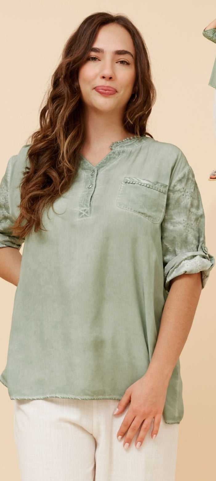 A woman modeling a light sage green long-sleeve blouse with a half-placket and chest pocket, paired with white pants, shown on a beige studio background with a smaller inset view of the full outfit.